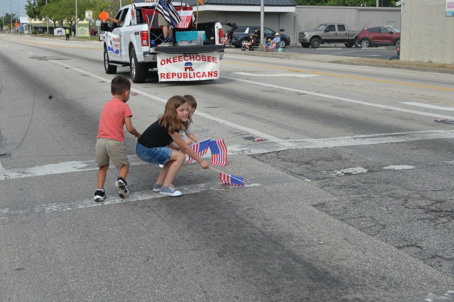 OKEECHOBEE -- Children pick up American flags that were tossed onto the pavement by the Republican Club's parade entry in the Speckled Perch Festival Parade. [Photo by Katrina Elsken/Lake Okeechobee News]